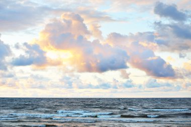 Gün batımında fırtınadan sonra Baltık Denizi kıyısında parlak pembe kümülüs bulutlarıyla dolu açık bir gökyüzü. Dramatik bulut manzarası. Sıcak altın güneş ışığı. Resimli bir manzara var. Huysuz hava