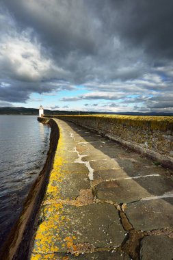 Eski deniz fenerine doğru boş bir gezinti, yakın plan. Arka planda kayalık kıyılar var. Dramatik bulut manzarası. Ardrishaig, Crinan Kanalı, İskoçya, İngiltere
