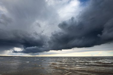 Gün batımında fırtınadan sonra Baltık Denizi kıyısında bir sürü koyu renkli kümülüs bulutu olan açık bir gökyüzü. Dramatik bulut manzarası. Resimli bir manzara var. Kararsız hava, mevsimler, iklim değişikliği