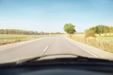 Açık bir günde tarla ve orman boyunca asfalt yol (karayolu). Sıcak gün ortası güneşi, açık gökyüzü. Arabadan bir manzara. Seyahat yerleri, tatiller, özgürlük, sürüş, ulaşım