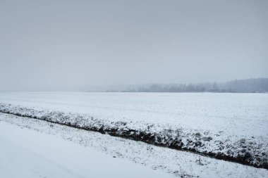 Kar fırtınasından sonra kırsal alanda karla kaplı bir yol. Elektrik hattı, trafo direkleri. Arabadan panoramik görüntü. Karanlık, fırtınalı bir gökyüzü. Off-road, lojistik, kış lastikleri, uzak köy
