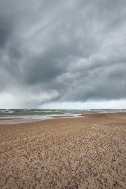 Fırtına sonrası dramatik bulutların altında Baltık Denizi 'nin kumlu sahili. Letonya 'da sızıntı var. Destansı deniz manzarası. Kasırga, fırtına, sert hava, meteoroloji, iklim değişikliği, doğal fenomen