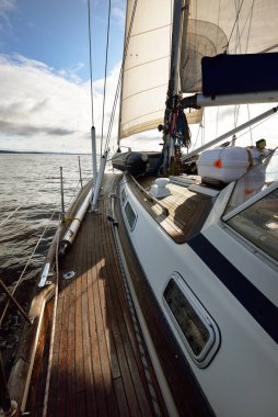 Bulutlu bir günde ahşap meşe güverteli, yelkenli, modern bir yat. Direğe ve yelkenlere bir manzara. Su, yakından sıçrıyor. Tarbert, İskoçya, İngiltere