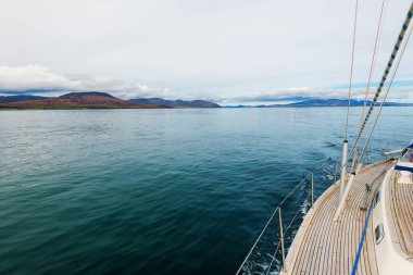 Bulutlu bir günde, Jura adasının kayalık kıyılarında seyir halindeki ahşap meşe güvertesiyle donatılmış modern bir yat. Inner Hebrides, İskoçya, İngiltere. Spor, eğlence, gezi, seyahat yerleri.