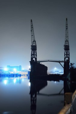 Kargo limanı terminali ve nehir gece. Gemi, vinç, depo. Aydınlatılmış Noel ağacı, arka planda ışıklar. Karanlık şehir manzarasını kavra. Sudaki simetri yansımaları