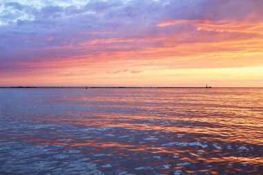 Gün batımında Baltık Denizi. Suya yansıyan parlayan bulutlarla dramatik bir gökyüzü. Arka planda deniz feneri var. Güneş batıyor. Destansı deniz manzarası. Soyut doğal desen, doku, arkaplan, konsept resim