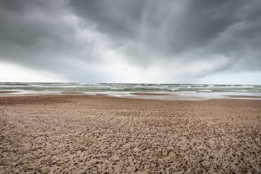 Fırtına sonrası dramatik bulutların altında Baltık Denizi 'nin kumlu sahili. Letonya 'da sızıntı var. Destansı deniz manzarası. Kasırga, fırtına, sert hava, meteoroloji, iklim değişikliği, doğal fenomen