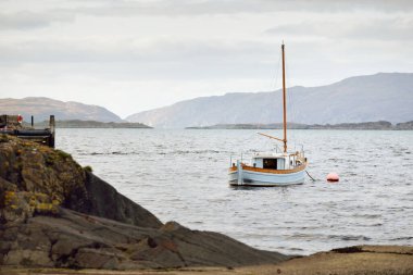 Bulutlu bir günde Crinan Kanalı 'nın kayalık kıyısında demirli tahta bir yat. Argyll ve Bute, İskoçya, İngiltere