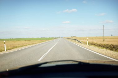 Açık bir günde kırsal alanlarda boş bir otoyol. Sıcak güneş ışığı, açık mavi gökyüzü. Arabadan bir manzara. Seyahat yerleri, tatiller, özgürlük, sürüş, ulaşım
