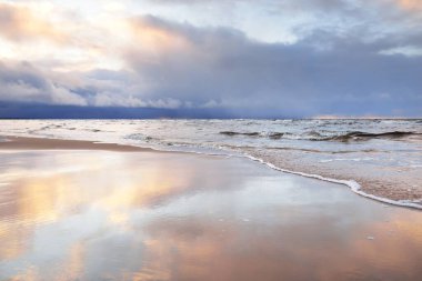 Kumlu bir sahilden Baltık Denizi 'nin panoramik manzarası. Açık günbatımı gökyüzü, parlak pembe bulutlar, yumuşak ışık. Suyun simetri yansımaları, doğal ayna. Hava, kış, iklim değişikliği, doğa