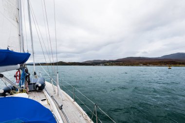 Bulutlu bir günde, Jura adasının kayalık kıyılarında seyir halindeki ahşap meşe güvertesiyle donatılmış modern bir yat. Inner Hebrides, İskoçya, İngiltere. Spor, eğlence, gezi, seyahat yerleri.