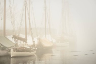 Zarif ve modern yatlar, yelkenli ve balıkçı tekneleri, kalın bir siste iskeleye demirlemiş küçük gemiler. Manzaralar, turistik yerler, eski liman, tarih, geçmiş. Sepia görüntü efekti. Germaniahafen, Kiel, Almanya