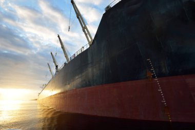 Gün batımında limana demir atmış büyük bir kargo gemisi. Vinçler arka planda. Riga, Baltık Denizi, Letonya. Yük taşımacılığı, küresel iletişim, lojistik, çevresel hasar