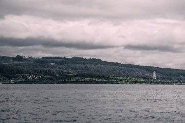 Dramatik gökyüzü altında Tarbert 'in kayalık kıyılarının panoramik manzarası. Arka planda deniz feneri, İskoçya, İngiltere. Seyahat yerleri, ulusal dönüm noktası, eğlence, eko turizm, tatiller