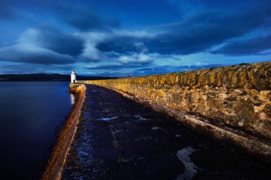 Gece eski deniz fenerine boş bir gezinti, yakın plan. Arka planda kayalık kıyılar var. Dramatik bulut manzarası. Ardrishaig, Crinan Kanalı, İskoçya, İngiltere. Seyahat yerleri, manzaralar, işaretler.