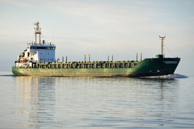 Büyük yeşil kargo gemisi gün batımında açık denizde yelken açıyor. Renkli parlayan bulutlar, sıcak güneş ışığı. Görüntüyü algıla. Nakliye, iş, ekonomi, sanayi, küresel iletişim, lojistik