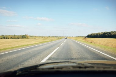 Açık bir günde kırsal alanlarda boş bir otoyol. Sıcak güneş ışığı, açık mavi gökyüzü. Arabadan bir manzara. Seyahat yerleri, tatiller, özgürlük, sürüş, ulaşım