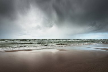 Fırtına sonrası dramatik bulutların altında Baltık Denizi 'nin kumlu sahili. Letonya 'da sızıntı var. Destansı deniz manzarası. Kasırga, fırtına, sert hava, meteoroloji, iklim değişikliği, doğal fenomen