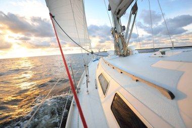 Gün batımında açık denizde yelken açmak. Güvertenin yakın görüntüsü, direk ve yelkenler. Yağmurdan sonra açık gökyüzü, çarpıcı parlayan bulutlar, altın güneş ışığı, dalgalar ve su sıçramaları, kasırga. Destansı deniz manzarası