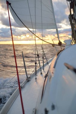 Gün batımında açık denizde yelken açmak. Güvertenin yakın görüntüsü, direk ve yelkenler. Yağmurdan sonra açık gökyüzü, çarpıcı parlayan bulutlar, altın güneş ışığı, dalgalar ve su sıçramaları, kasırga. Destansı deniz manzarası