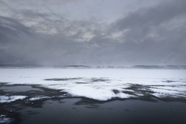 Karla kaplı tarım tarlaları ve ormanlar dramatik bir gökyüzü altında. Kar fırtınası. Traktör rayları, elektrik hattı, trafo direklerine yakın çekim. Kırsal kesimde kış manzarası. Doğa, çevre, uzak yerler