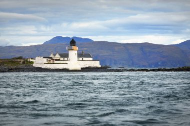 Jura adasının batı kıyısının kayalık kıyıları, yatın manzarası. Beyaz deniz feneri yakın plan. Fırtınadan sonra dramatik bulutlar. Inner Hebrides, İskoçya, İngiltere. Atmosferik manzara