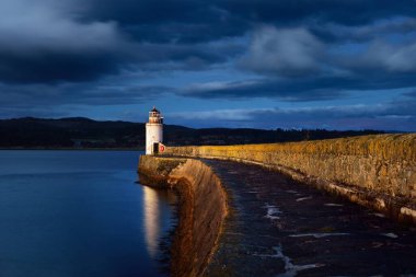 Gece eski deniz fenerine boş bir gezinti, yakın plan. Arka planda kayalık kıyılar var. Dramatik bulut manzarası. Ardrishaig, Crinan Kanalı, İskoçya, İngiltere. Seyahat yerleri, manzaralar, işaretler.