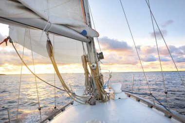Günbatımında yağmurdan sonra beyaz yat denize açılacak. Güverteden pruvaya kadar yakın çekim. Renkli altın ve pembe bulutlarla parlayan parlak bir gökyüzü. Idyllic deniz manzarası. Deniz, seyahat, seyahat yerleri
