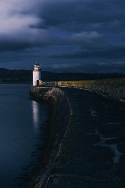 Gece eski deniz fenerine boş bir gezinti, yakın plan. Arka planda kayalık kıyılar var. Dramatik bulut manzarası. Ardrishaig, Crinan Kanalı, İskoçya, İngiltere. Seyahat yerleri, gezi teması