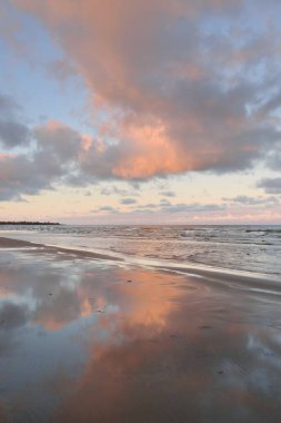 Kumlu bir sahilden Baltık Denizi 'nin panoramik manzarası. Açık günbatımı gökyüzü, parlak pembe bulutlar, yumuşak ışık. Suyun simetri yansımaları, doğal ayna. Hava, kış, iklim değişikliği, doğa