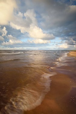 Gün batımında fırtınadan sonra Baltık kıyıları üzerinde parlayan kümülüs bulutlarıyla açık bir gökyüzü. Dramatik bulut manzarası. Sıcak altın güneş ışığı. Resimli bir manzara var. Hava kararsız. Uzun pozlama