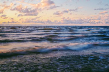 Gök gürültülü bir fırtınadan sonra denizin üstünde destansı pembe gün batımı bulutları. Dramatik bir gökyüzü. Dalgalar ve su dokuya sıçrar. Idyllic deniz manzarası. Kavramsal görüntü, uzun pozlama. Resim gibi bir manzara.