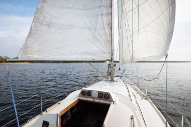 Rüzgardan kanat çırpan yelkenli beyaz bir yat fırtınadan sonra yelken açıyor. Güverteden pruvaya kadar yakın çekim. Boş zaman aktivitesi, spor, eğlence teması. Glomma Nehri, Oslofjord, Norveç
