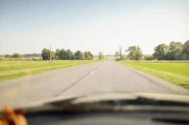 Açık bir günde tarla ve orman boyunca asfalt yol (karayolu). Sıcak gün ortası güneşi, açık gökyüzü. Arabadan bir manzara. Seyahat yerleri, tatiller, özgürlük, sürüş, ulaşım