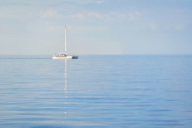 Beyaz modern yat (katamaran) gün batımında açık bir Karayip denizinde yüzüyor. Açık mavi gökyüzü, suda simetri yansımaları. Idyllic deniz manzarası. Seyahat yerleri, spor, boş zaman aktivitesi, dinlenme