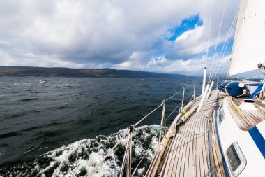 Teknelerle donatılmış modern bir yat. Tahta meşe güverteli. Clyde Nehri Firth 'ün kayalık kıyılarına doğru yol alıyorlar. Dramatik bir gökyüzü. İskoçya, İngiltere. Seyahat yerleri, eko turizm, tatiller, saf doğa.