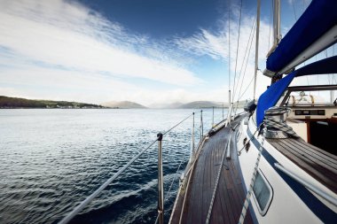 Fırtına gökyüzü. Tekne hileli modern yat, tahta meşe güvertesiyle Clyde 'ın Fırtınası' nda yelken açıyor. Arka planda Bute Adası 'nın ormanları, tepeleri ve dağları var. İskoçya, İngiltere