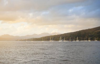 Göz kamaştırıcı gün batımı bulutları. Küçük bir köy olan Rhu, İskoçya, İngiltere kıyısında demirli yelkenliler ve ahşap botlar.