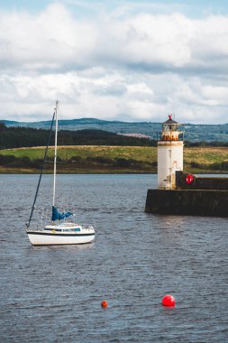 Bulutlu bir günde yelken açan küçük bir yat, yakın plan. Arka planda kayalık kıyılar var. Dramatik bulut manzarası. Ardrishaig, Crinan Kanalı, İskoçya, İngiltere. Seyahat yerleri, spor, eğlence.