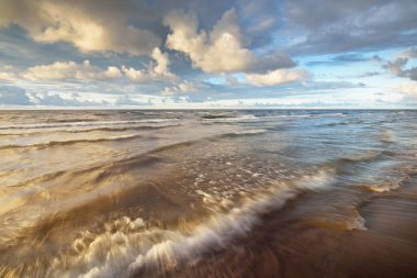 Gün batımında fırtınadan sonra Baltık kıyıları üzerinde parlayan kümülüs bulutlarıyla açık bir gökyüzü. Dramatik bulut manzarası. Sıcak altın güneş ışığı. Resimli bir manzara var. Hava kararsız. Uzun pozlama