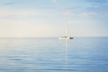 Beyaz modern yat (katamaran) gün batımında açık bir Karayip denizinde yüzüyor. Açık mavi gökyüzü, suda simetri yansımaları. Idyllic deniz manzarası. Seyahat yerleri, spor, boş zaman aktivitesi, dinlenme