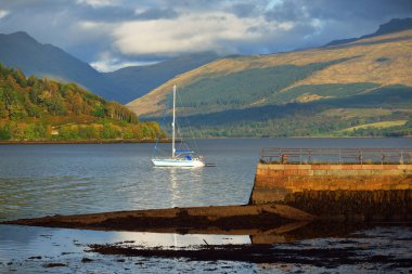 Loch Fyne yakınlarındaki sahil, orman ve tepelerin manzarası. Beyaz yelkenli yatla yakın plan. Inveraray, Inner Hebrides, Argyll ve Bute, İskoçya, İngiltere