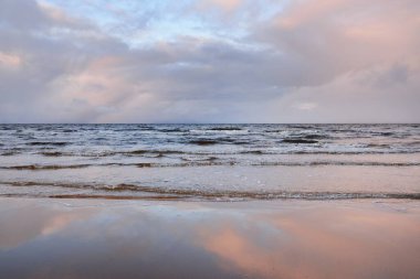 Kumlu bir sahilden Baltık Denizi 'nin panoramik manzarası. Açık günbatımı gökyüzü, parlak pembe bulutlar, yumuşak ışık. Suyun simetri yansımaları, doğal ayna. Hava, kış, iklim değişikliği, doğa