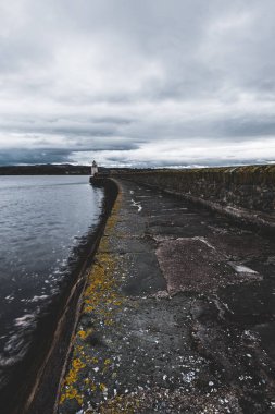 Eski deniz fenerine doğru boş bir gezinti, yakın plan. Arka planda kayalık kıyılar var. Dramatik bulut manzarası. Ardrishaig, Crinan Kanalı, İskoçya, İngiltere. Seyahat yerleri, gezi teması