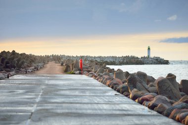 Gün batımında deniz fenerine boş bir yaya geçidi (gezinti güvertesi). Dalgakıranlar yakın çekim. Baltık Denizi, Ventspils, Letonya. Boş zaman aktivitesi, spor, eğlence, kuzey yürüyüşü, seyahat yerleri