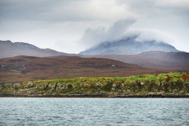 Jura adasının kıyılarının panoramik manzarası, dağları ve vadileri sudan. Bulutlu mavi gökyüzü. Fırtınalı hava. Paps of Jura, Inner Hebrides, İskoçya, İngiltere