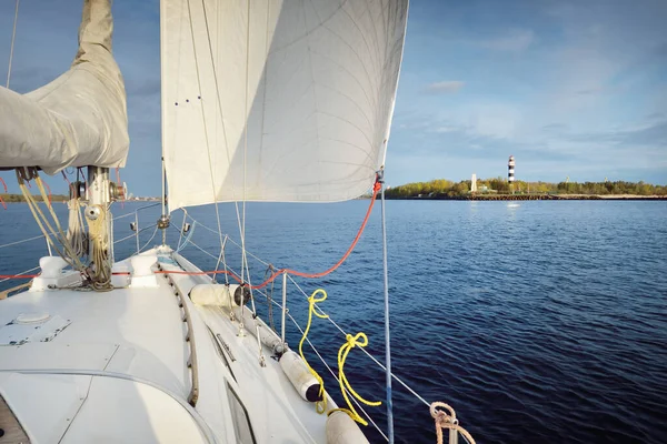 White yacht sailing in the Baltic sea after the rain at sunset. Riga, Latvia. Close-up view from the deck to the bow, mast and sails. Lighthouse in the background. Sport, recreation, travel