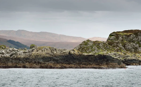 Jura adasının kıyılarının panoramik manzarası, dağları ve vadileri sudan. Bulutlu mavi gökyüzü. Fırtınalı hava. Paps of Jura, Inner Hebrides, İskoçya, İngiltere