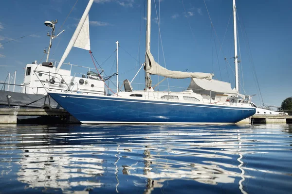 Classic blue sloop rigged yacht moored in marina with a sun cover. Cruising life, vacation, sailboat travel, sailing, recreation, leisure activity, sport, transportation, water surface texture