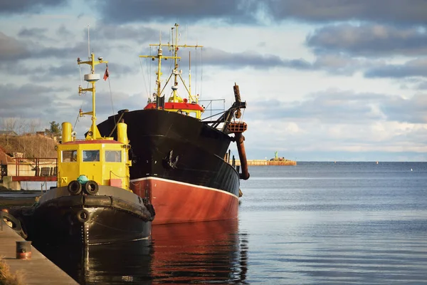 Small ship and fishing boat moored to a pier in a harbor at sunset. Baltic sea, Latvia. Idyllic winter seascape. Industry, business, transportation, service, logistics, delivery, shipping